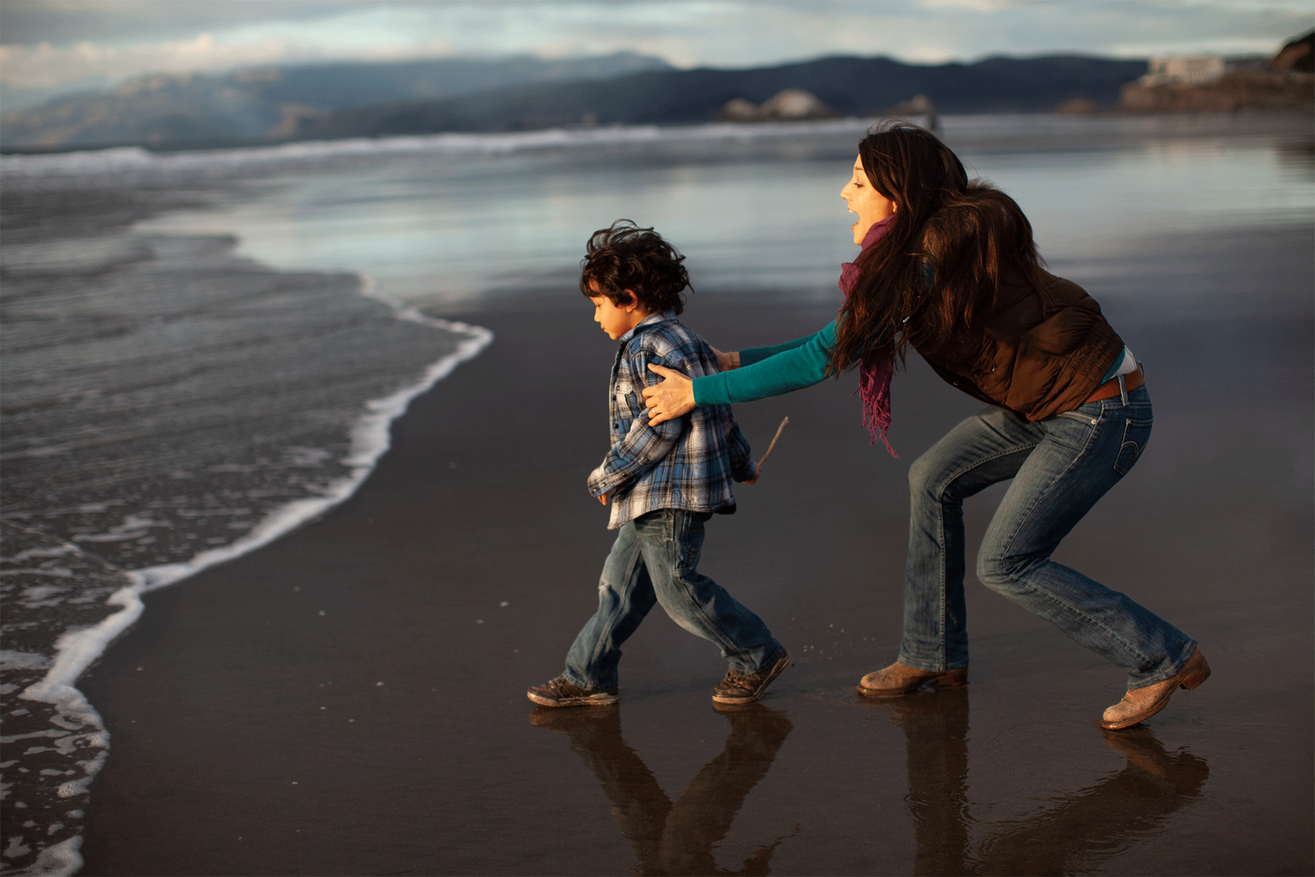A woman and her son play at the edge of the ocean