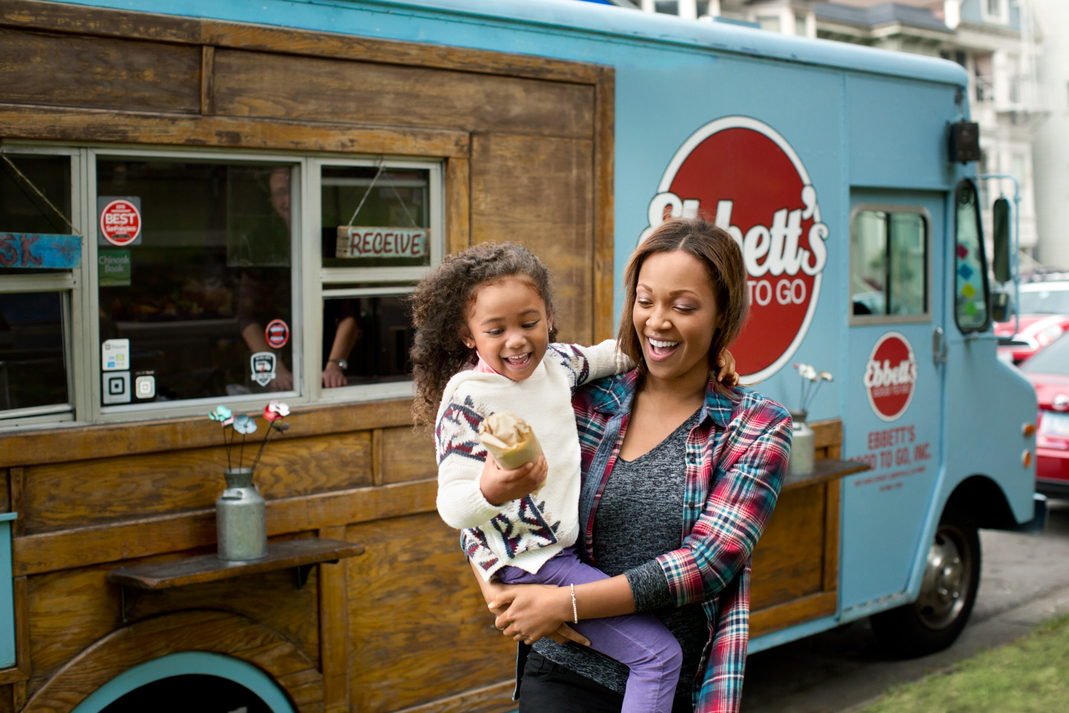 A woman and her daughter buy a sandwich from a food truck