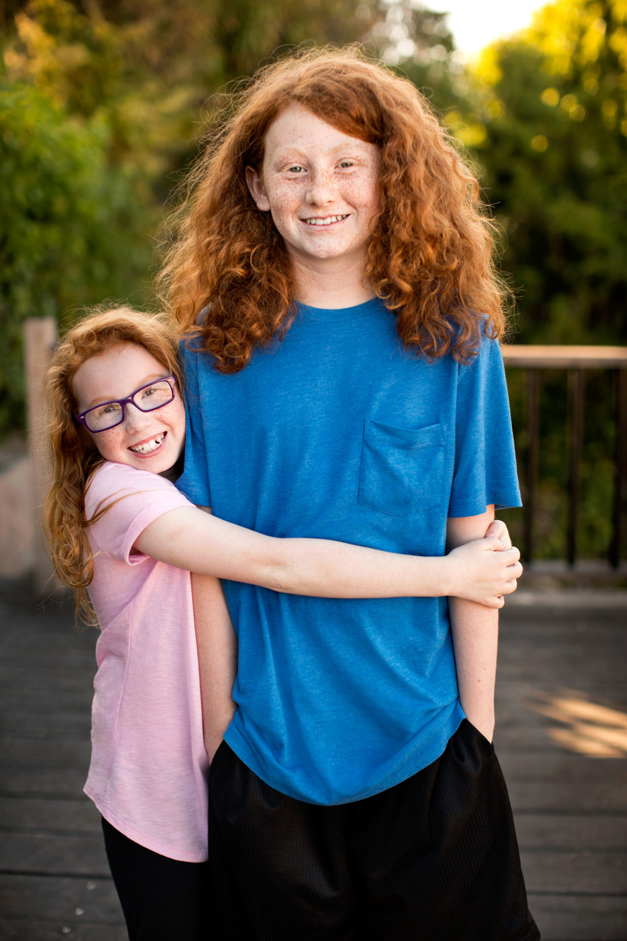 A red haired girl in a pink t-shirt hugs her older brother
