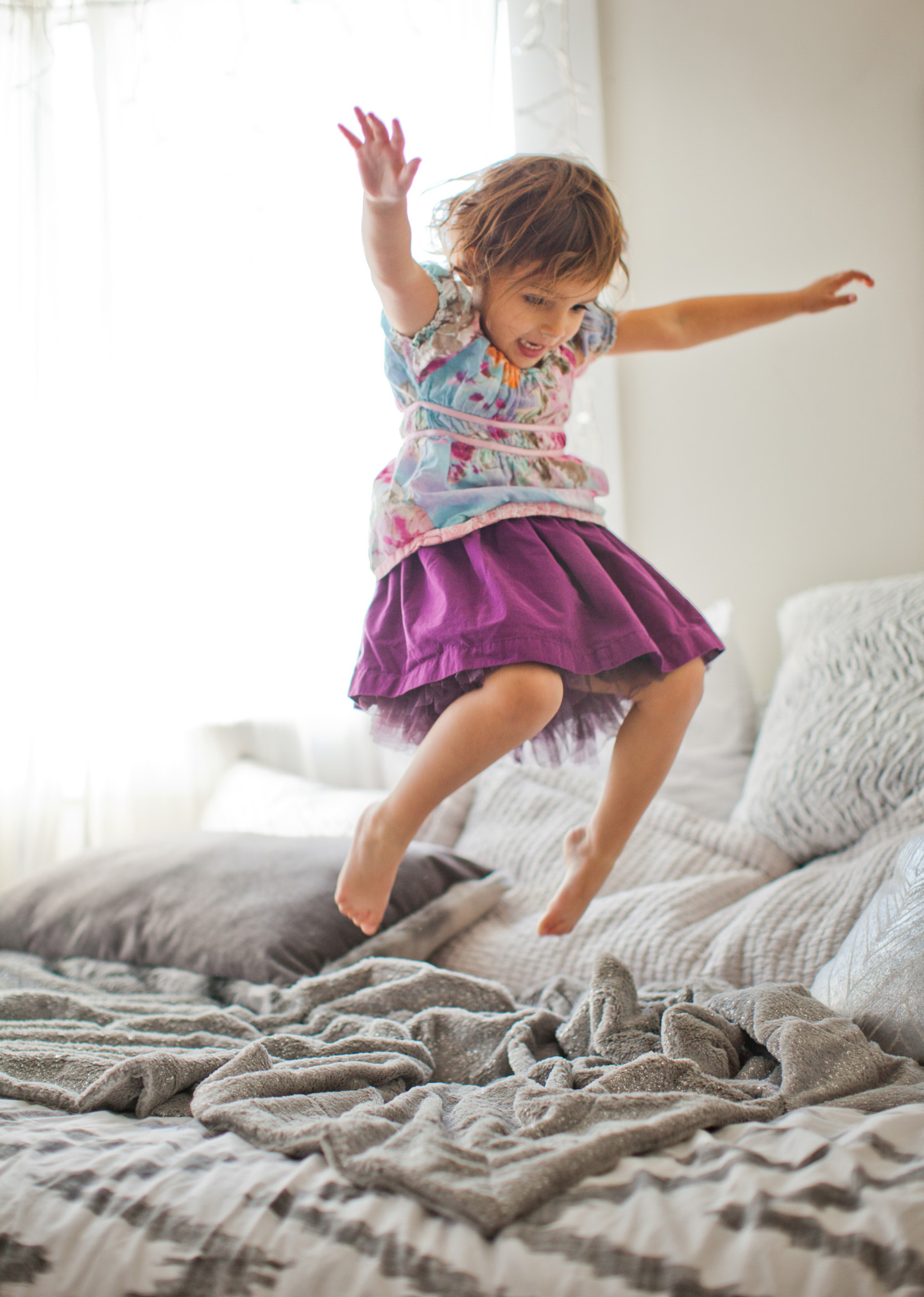 A 5-year-old girl in a purple tutu jumps on a bed