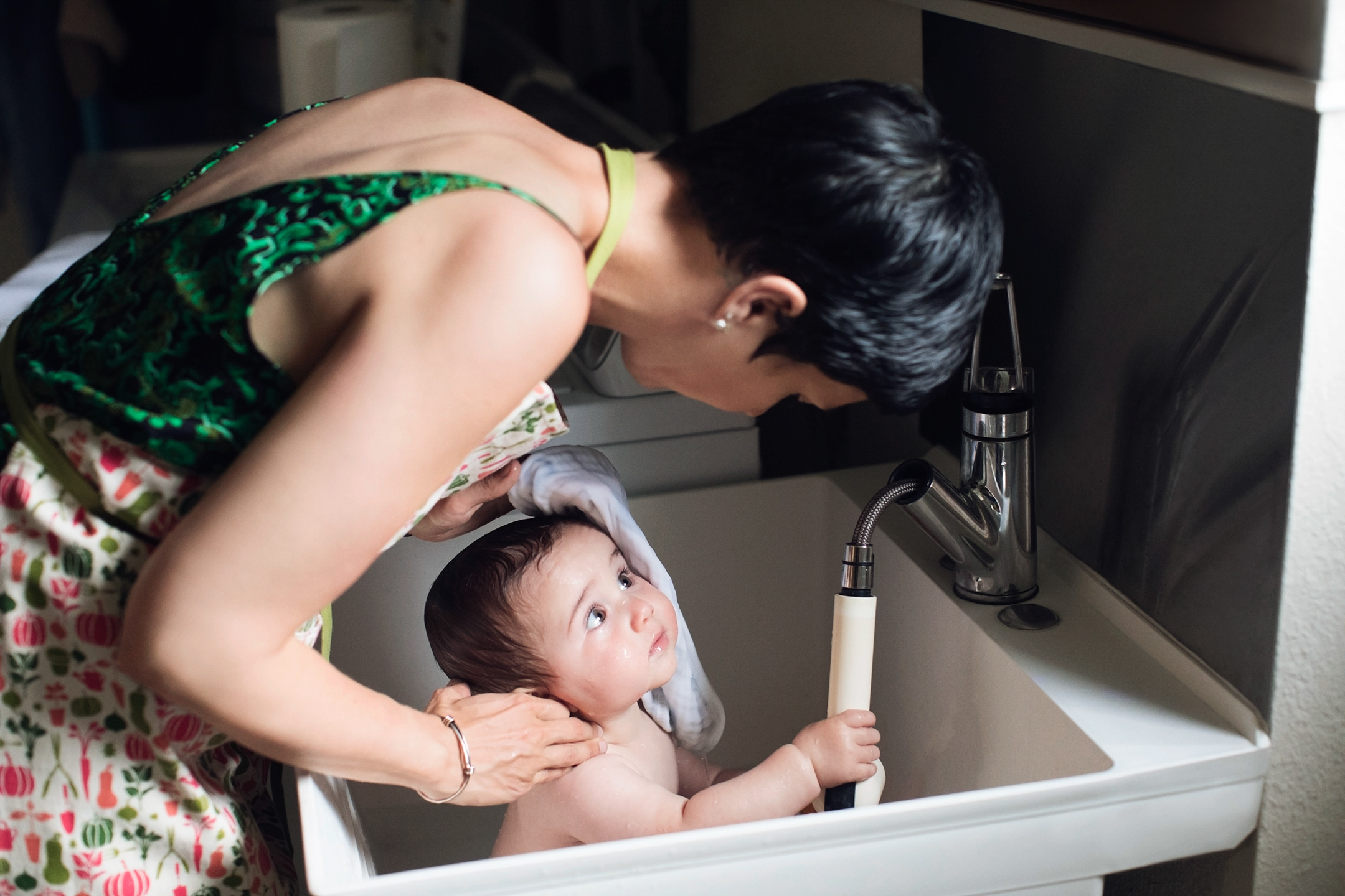 A woman bathes her infant son in a laundry room sink