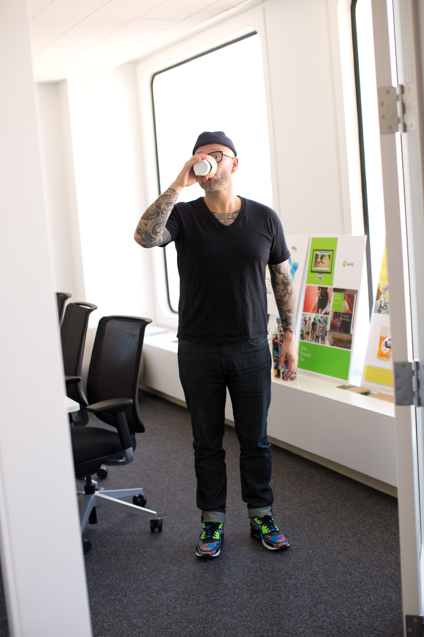A man with tattoos and trainers drinks coffee in a San Francisco office