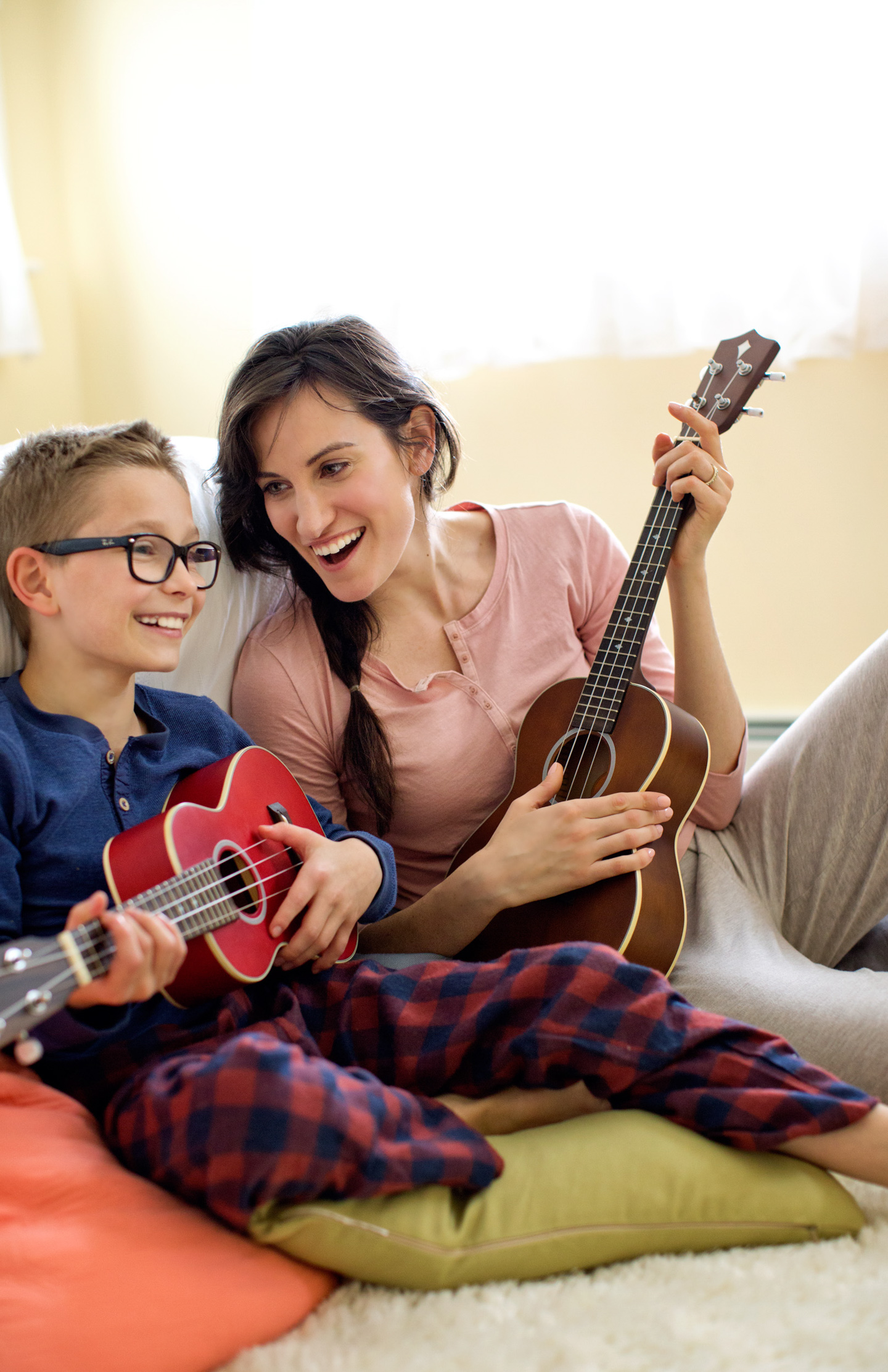 A woman + her son play ukulele together in a bedroom