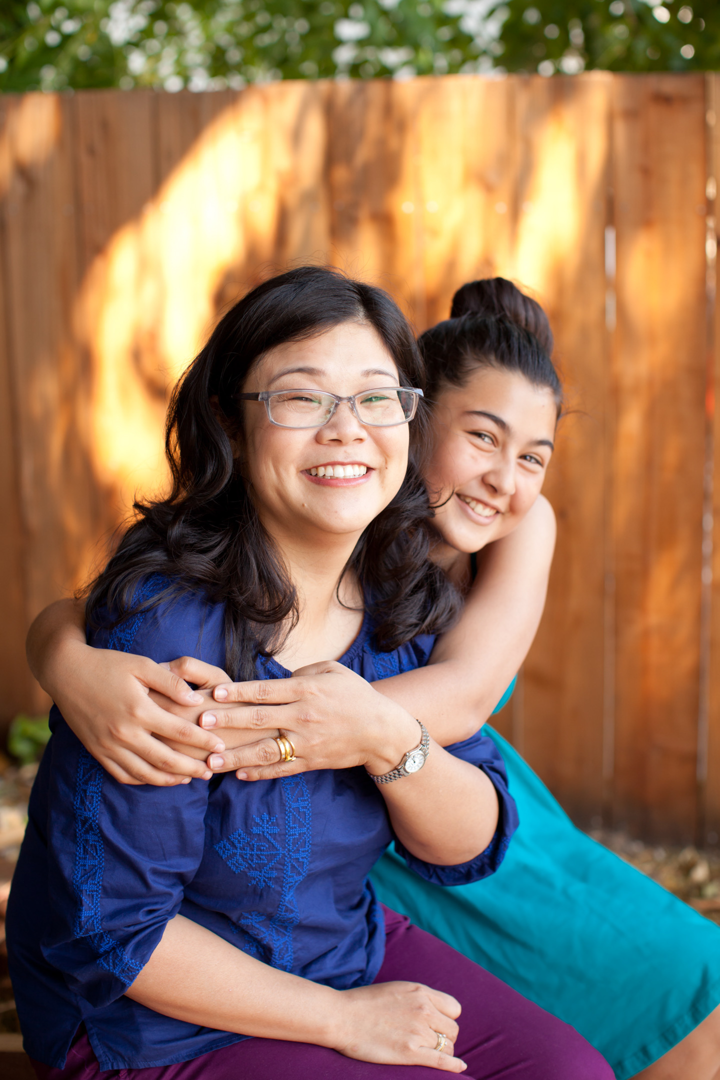 A teen girl hugs her mother while posing for a portrait in a garden
