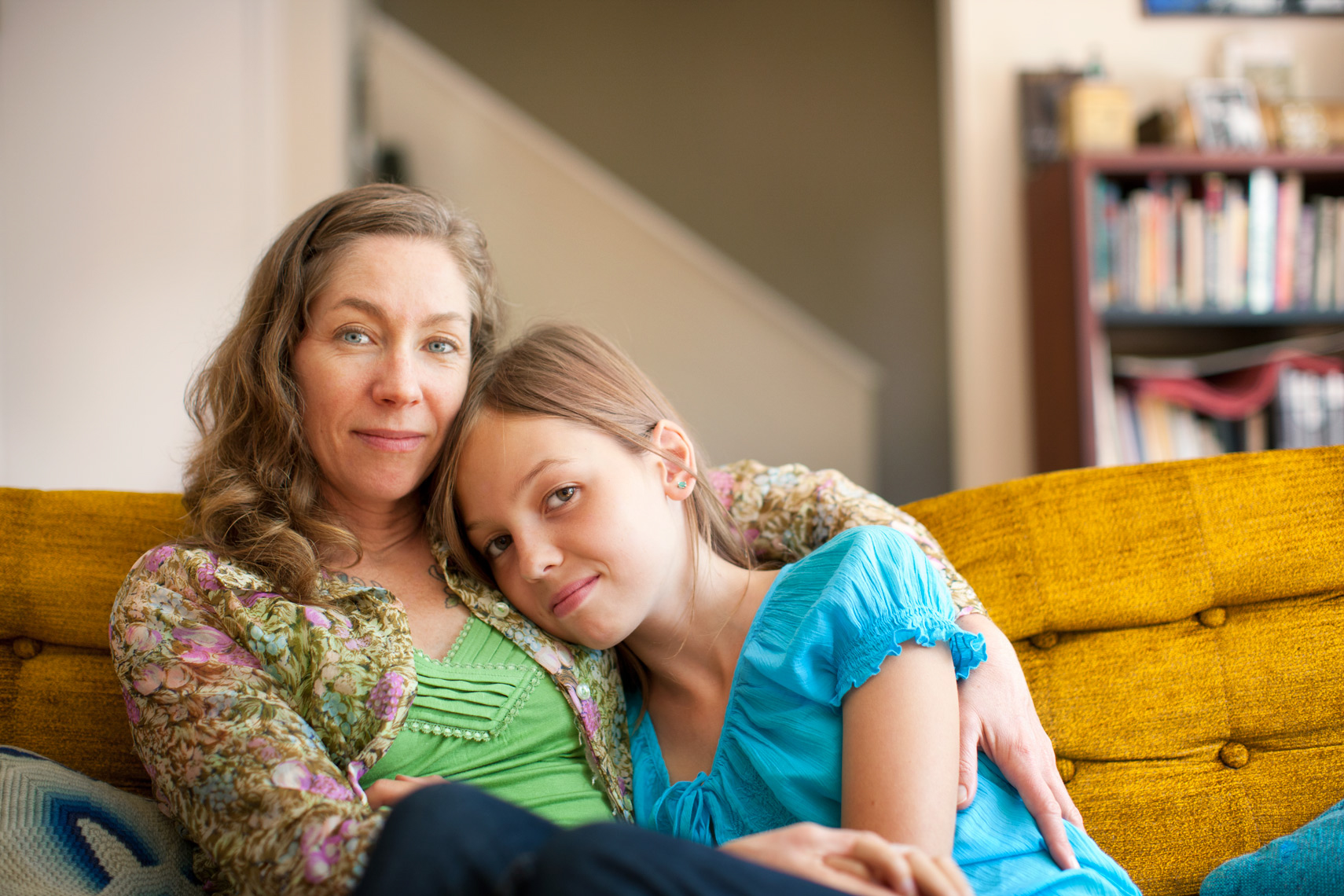 Portrait of a mother and her 12-year-old daughter sitting on a yellow velvet sofa