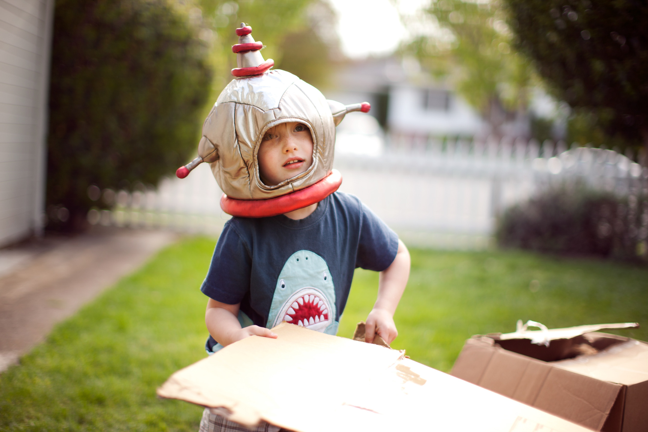 A boy in an astronaut helmet plays with a cardboard box