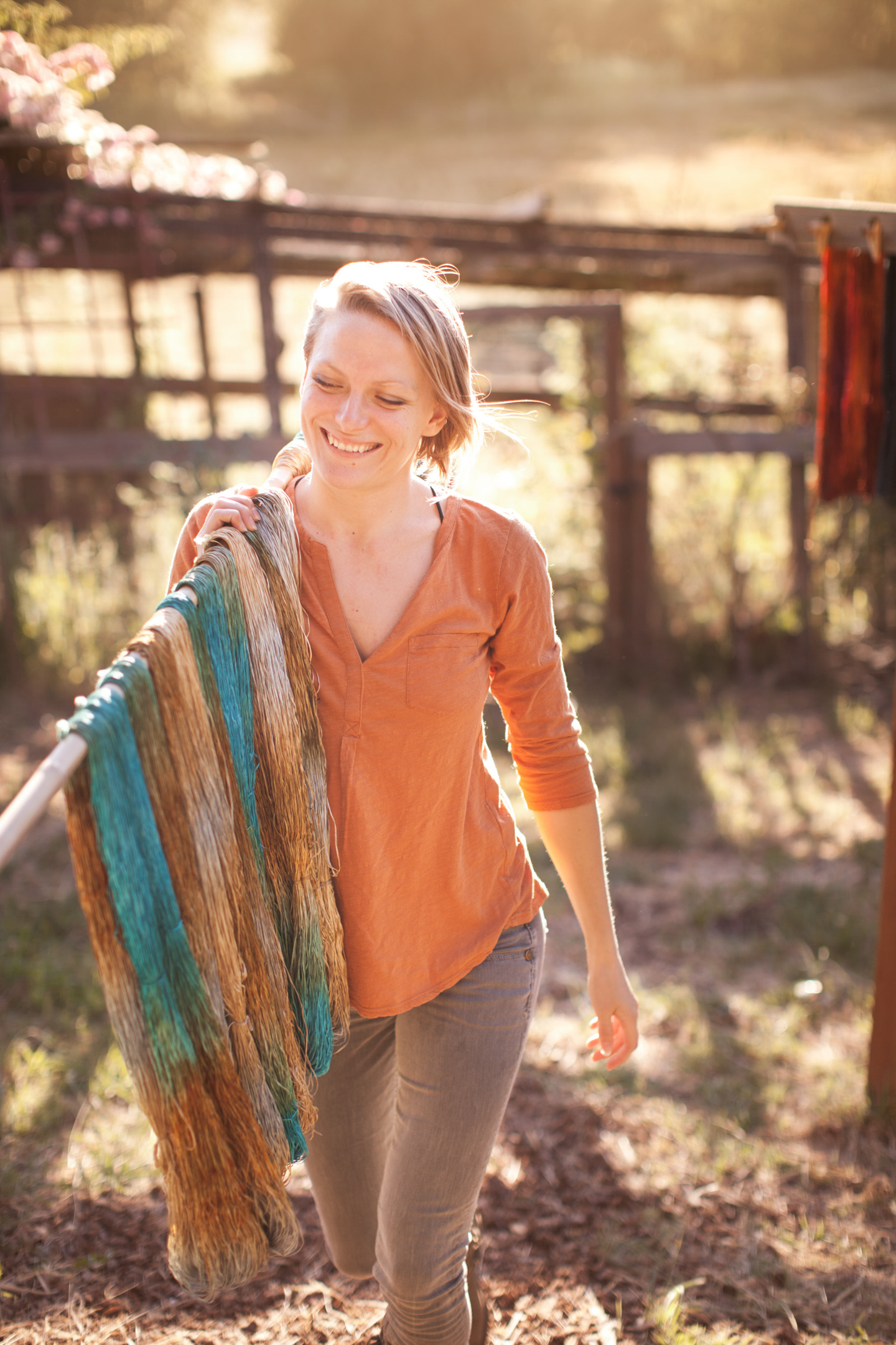 A woman carrying newly dyed yarn walks across a farmyard