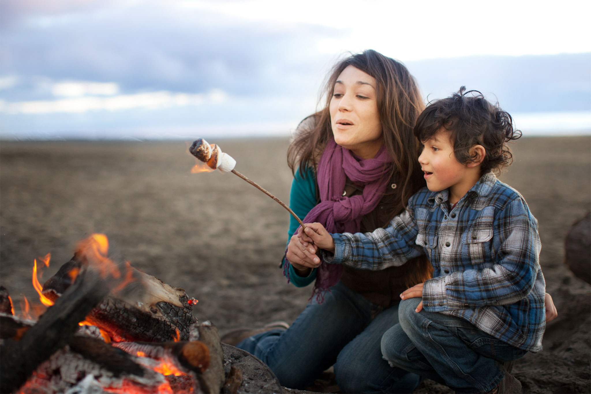 A woman and her son roast marshmallows over a fire at the beach