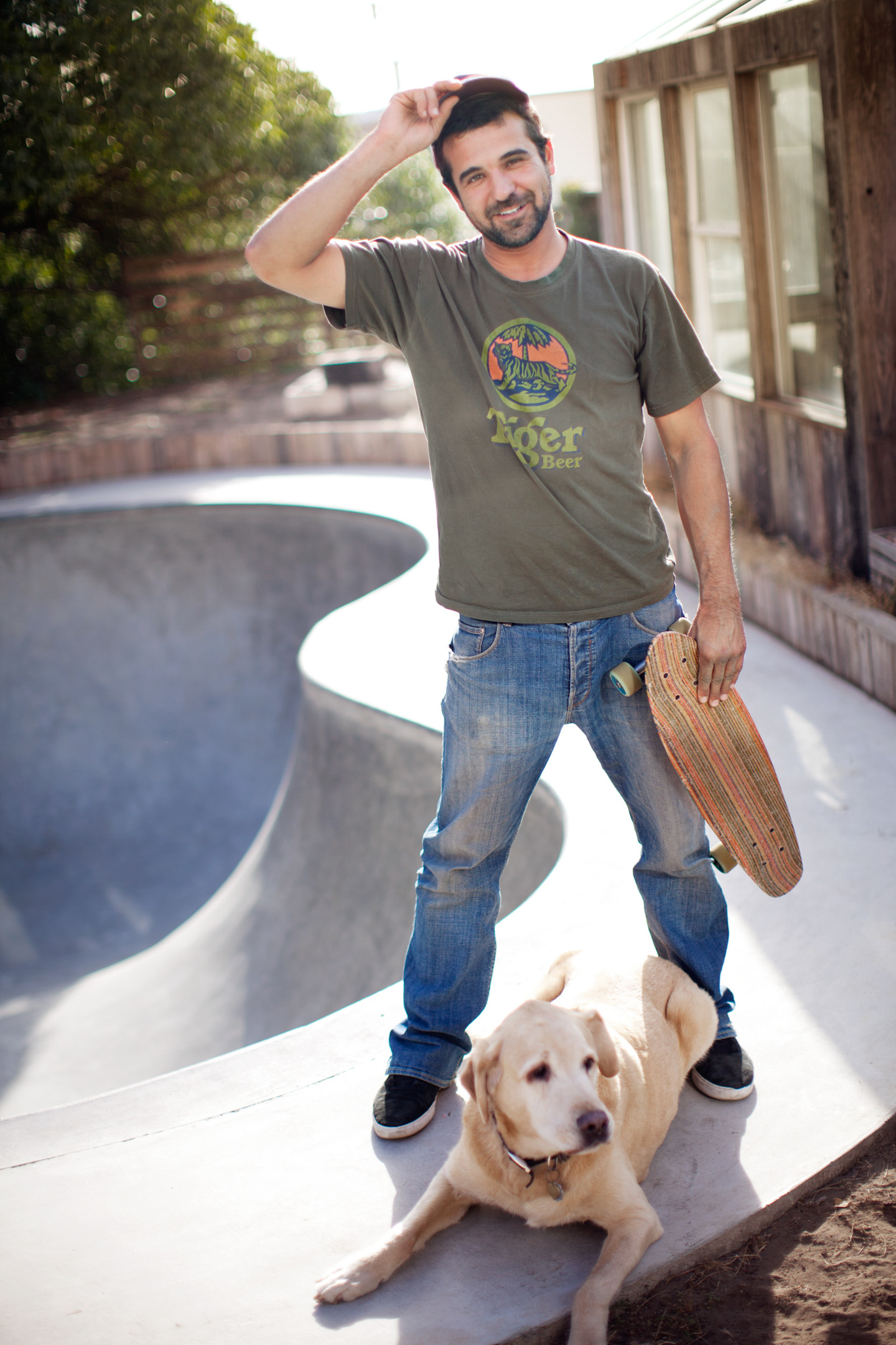 A skateboarder poses for a portrait with his dog in front of his backyard skate bowl