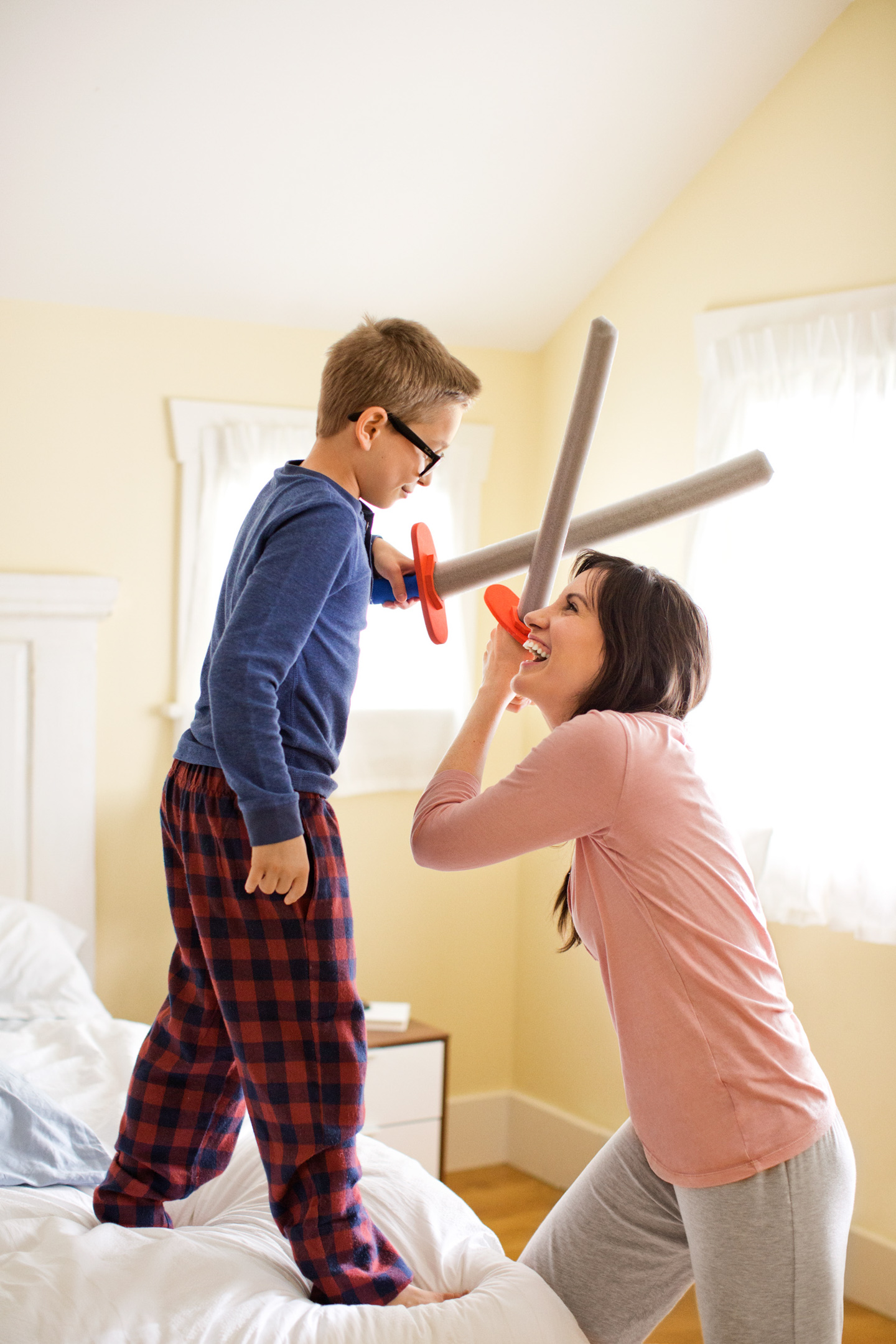 A woman and her son play a game of swords in their bedroom in the morning