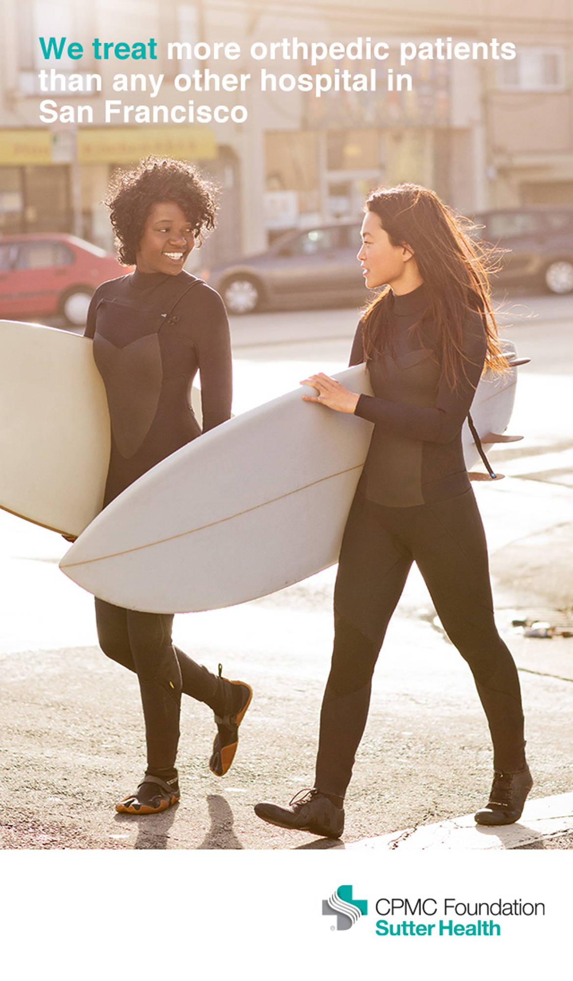 Two women carrying surfboards walk along a city street in a Healthcare Ad Campaign photographed by Lifestyle Photographer Diana Mulvihill