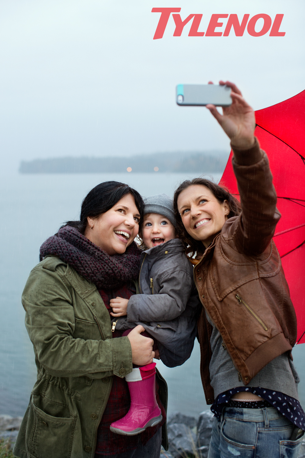 Two women take a selfie in the rain with their toddler daughter in a Tylenol Ad Campaign photographed by Lifestyle Photographer Diana Mulvihill